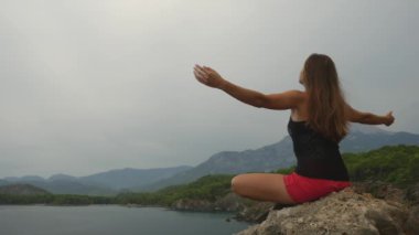 Kadın turist açık gökyüzü ve sakin deniz arka plan üzerinde bir kaya üzerinde oturan