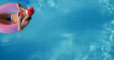 Woman in santa hat relaxing in a pool on the pink inflatable ring