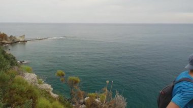 Hiker looking to the beatifull sea view. Young man tourist with a backpack standing on top of a mountain.