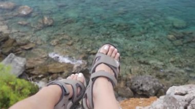 Young brave woman sitting on a high cliff above calm sea