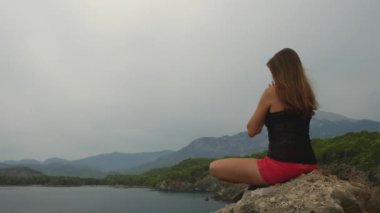 Kadın turist açık gökyüzü ve sakin deniz arka plan üzerinde bir kaya üzerinde oturan