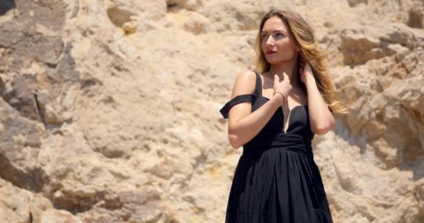 岩の上に深いカットアウトエレガントな黒いドレスを持つ美しい女性 — ストック動画