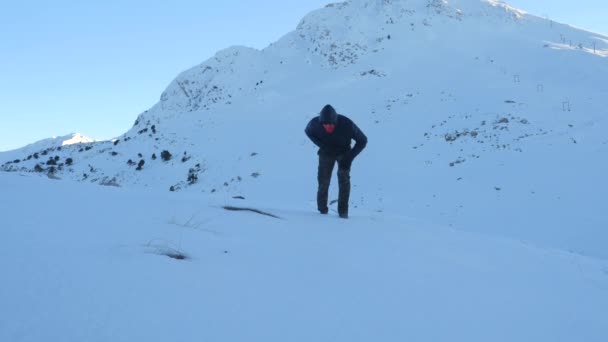 暗い服を着た若い男が雪に覆われた山で疲れ果てて — ストック動画