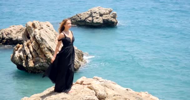 Giovane bella donna in abito nero ritaglio elegante seduta vicino al mare — Video Stock