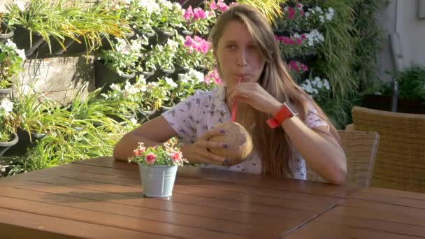 Jeune femme assise à la table avec une boisson à la noix de coco — Video