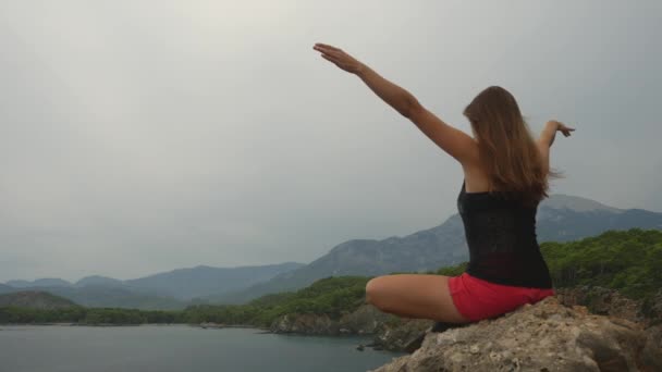 Kvinnlig turist sitter på en klippa på klar himmel och lugn havs bakgrund — Stockvideo