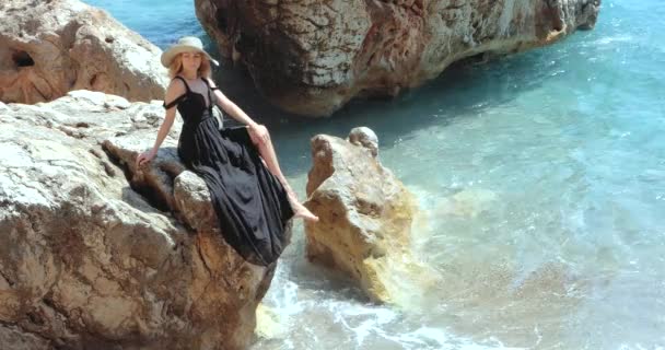 Jovem mulher bonita em preto vestido elegante sentado nas rochas perto do mar — Vídeo de Stock