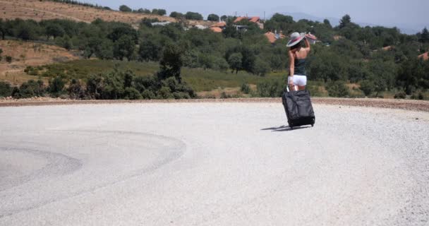 Joven mujer en pantalones cortos blancos va solo a lo largo de la carretera con el equipaje — Vídeos de Stock