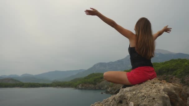 Kadın turist açık gökyüzü ve sakin deniz arka plan üzerinde bir kaya üzerinde oturan — Stok video