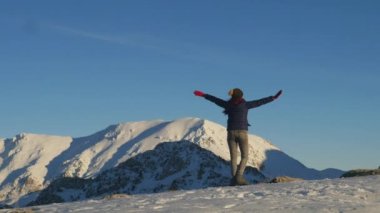 Young woman spinning around against sky and winter mountains
