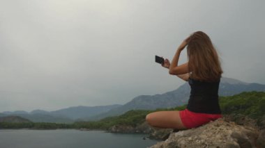Kadın turist açık gökyüzü ve sakin deniz arka plan üzerinde bir kaya üzerinde oturan