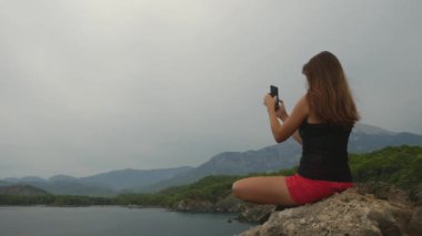 Kadın turist açık gökyüzü ve sakin deniz arka plan üzerinde bir kaya üzerinde oturan