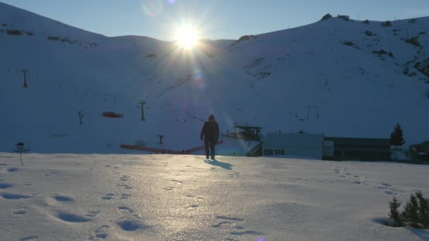 暗い服を着た若い男がゆっくりと雪の山を歩く — ストック動画