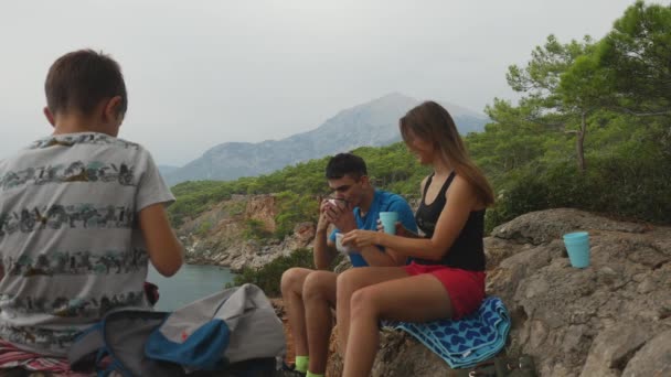 Семья сидит на скалах в лесу и ест пикник — стоковое видео