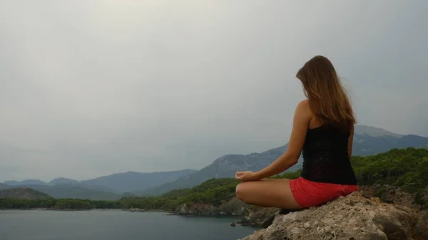 Turista sentada en una roca sobre un cielo despejado y un fondo marino tranquilo —  Fotos de Stock