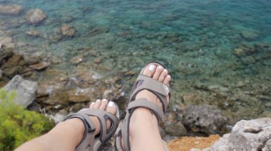 Young brave woman sitting on a high cliff above calm sea
