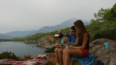 Young couple sitting on rocks in forest eating picnic
