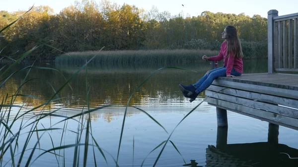 Jonge vrouw in roze pullower zittend op houten steiger over het water — Stockfoto