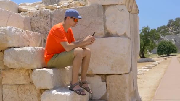 Jonge man zittend in het oude Agora op archeologische site van Patara. — Stockvideo