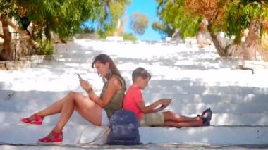 Young woman with boy sitting on stairs looking at smartphones
