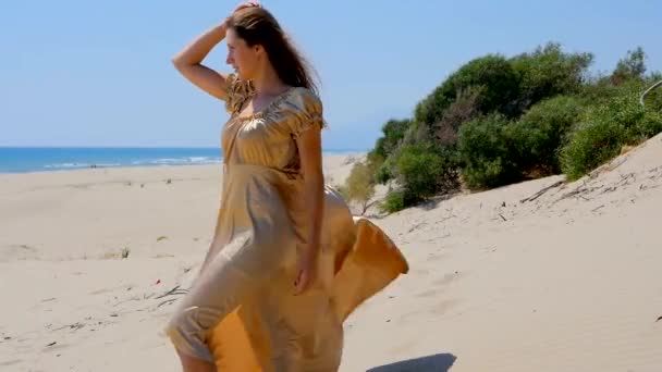 Mladá krásná žena ve zlatých dlouhých šatech stojící na písečných dunách v blízkosti moře. — Stock video