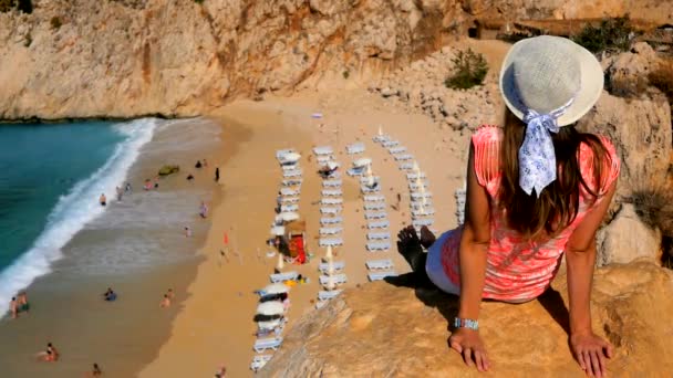Женщина, сидящая на скале над песчаным пляжем — стоковое видео