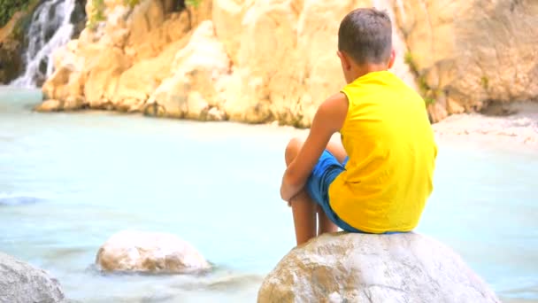 Вид ззаду дитини, що сидить на камені — стокове відео
