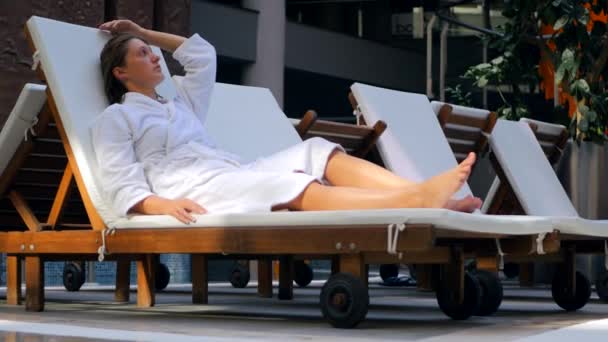 Young woman in bathrobe on the sunbed intdoors — Stockvideo