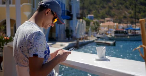 Молодой человек с мобильным телефоном в кафе на открытом воздухе — стоковое видео