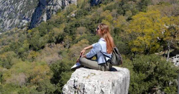 Young woman traveler sits on the rock — Stockvideo