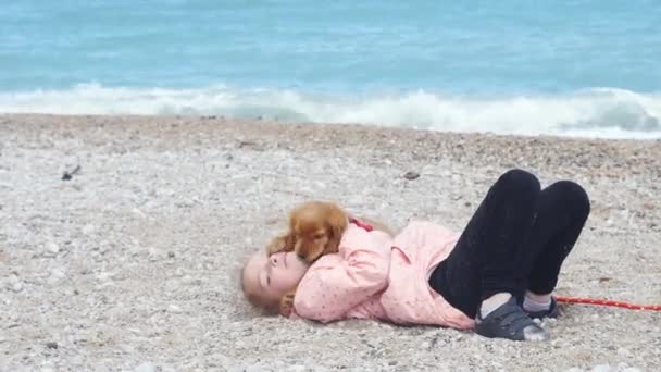 Petite fille allongée sur le sable avec son chiot doux — Video