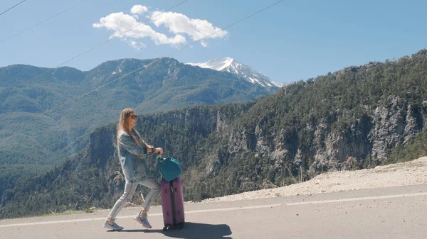 Güneşli bir günde açık havada valiz otostop ile kırsal yolda güzel genç bayan