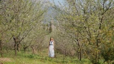 Bahar çiçekleri bahçesinde duran uzun elbiseli güzel bir kadın.