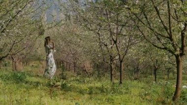 Bahar çiçekleri bahçesinde duran uzun elbiseli güzel bir kadın.