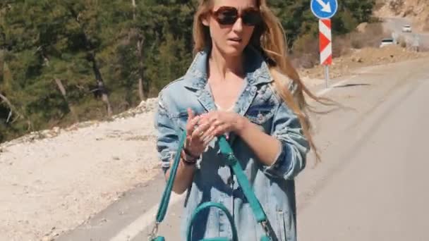 Όμορφη νεαρή κυρία με τζιν ρούχα κρατώντας μεγάλη τσάντα οτοστόπ ηλιόλουστη μέρα σε εξωτερικούς χώρους — Αρχείο Βίντεο