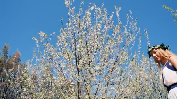 Νεαρή όμορφη γυναίκα με μακρύ φόρεμα στέκεται στον κήπο άνοιξη άνθος — Αρχείο Βίντεο