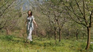 Bahar çiçekleri bahçesinde yürüyen uzun elbiseli güzel bir kadın.