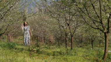 Bahar çiçekleri bahçesinde duran uzun elbiseli güzel bir kadın.
