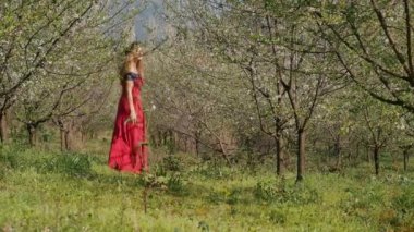 Bahar çiçekleri bahçesinde yürüyen uzun elbiseli güzel bir kadın.