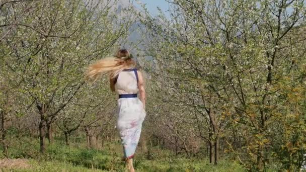 Joven hermosa mujer en vestido largo saltando en el jardín de flores de primavera — Vídeo de stock