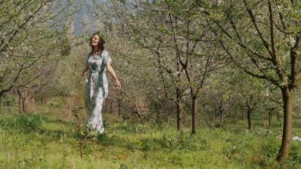 Fiatal gyönyörű nő hosszú ruhában séta a tavaszi virágos kertben — Stock videók