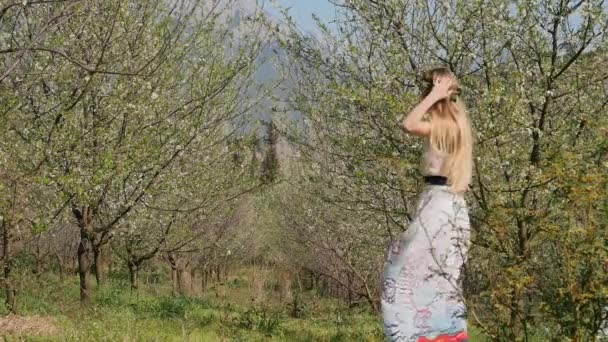 Young beautiful woman in long dress jumping in spring blossom garden — 비디오