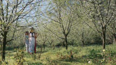 Bahar çiçekleri bahçesinde yürüyen uzun elbiseli güzel kadınlar.