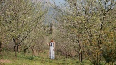 Bahar çiçekleri bahçesinde duran uzun elbiseli güzel bir kadın.