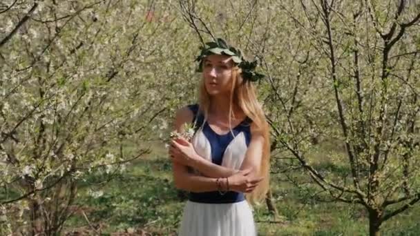 Молодая красивая женщина в длинном платье стоит в весеннем цветущем саду — стоковое видео