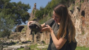 Yeşil tişörtlü genç bir kadın elinde yaşlı kaplumbağa tutuyor.
