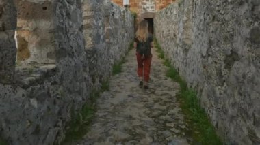 Kadın turist arka planda sakin Akdeniz manzaralı bir resim çekmek için antik kale duvarında yürüyor.