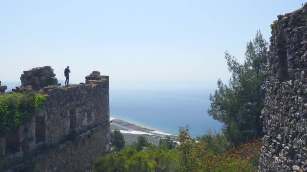 Άνθρωπος τουριστικός περπάτημα σε αρχαίο τοίχο κάστρο για να πυροβολήσει μια εικόνα με ήρεμη Μεσόγειο θάλασσα στο παρασκήνιο. — Αρχείο Βίντεο