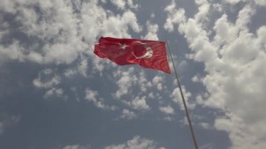 Arka planda mavi gökyüzü ile bayrak direğinde Türkiye Cumhuriyeti'nin rüzgar bayrağı sallayarak
