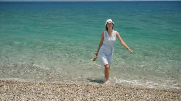 Giovane bella ragazza caucasica con cappello bianco passeggiate lungo la spiaggia vista costiera — Video Stock